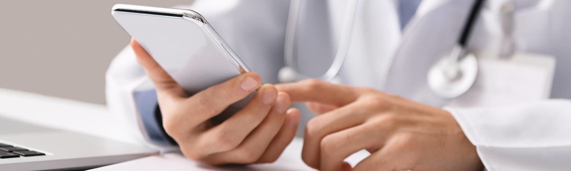Male doctor using smartphone at workplace, making online consultation