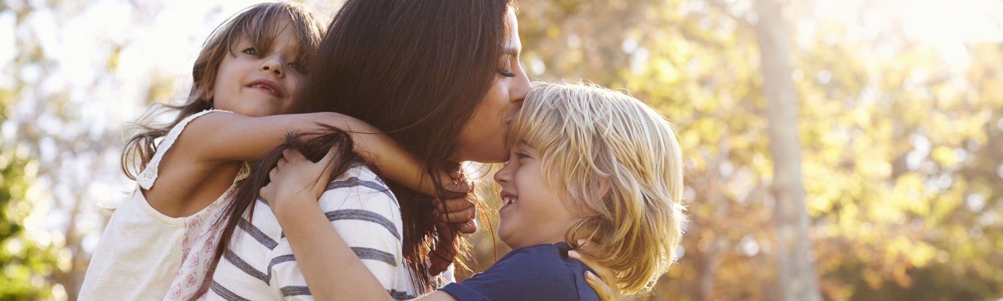 Mother Carrying Son And Daughter As They Play In Park